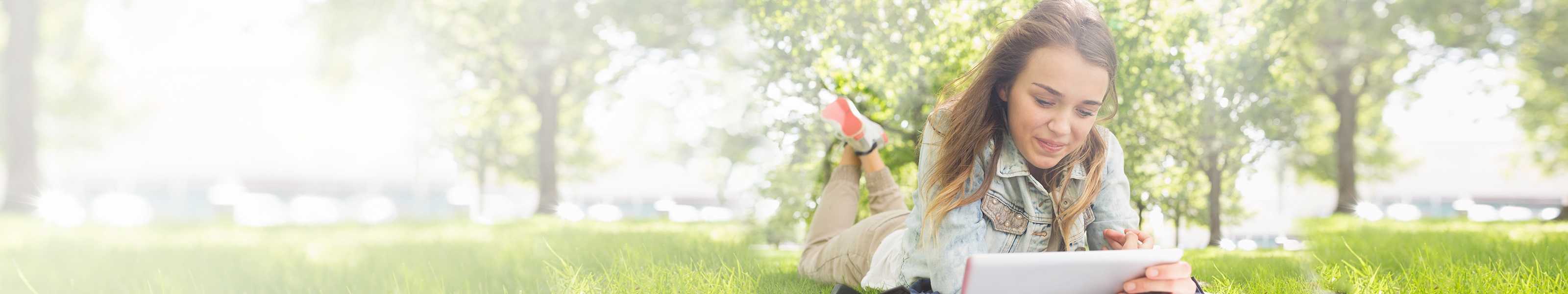 Young college-aged woman lies on grass while studying.