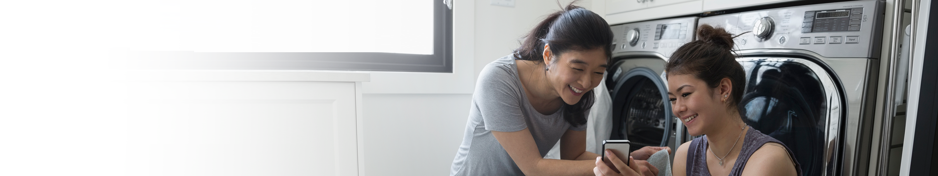 women looking at phone while sitting in front of washing machines