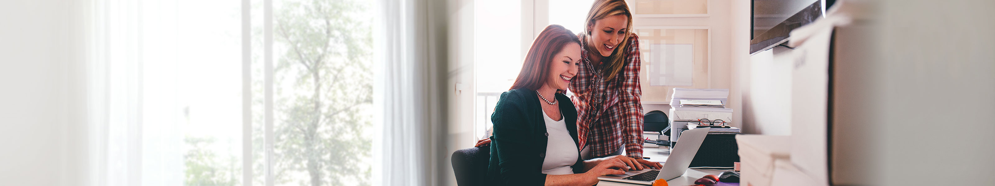 Two female coworkers are looking at something amusing on a laptop.